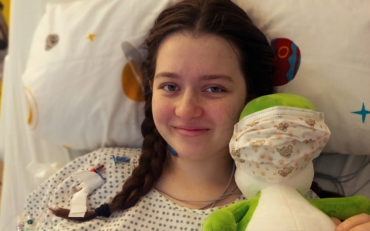 Młoda dziewczyna w szpitalu z maskotką, uśmiechająca się.