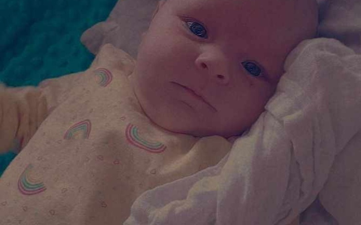 Noworodek leżący na kocyku, z wyrazem twarzy.