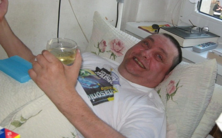 Mężczyzna leżący na łóżku, trzymający kieliszek z uśmiechem.