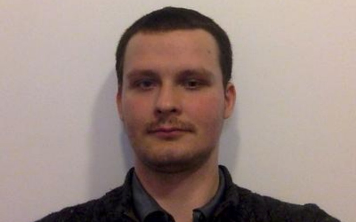 Mężczyzna pozujący do zdjęcia, z neutralnym wyrazem twarzy.