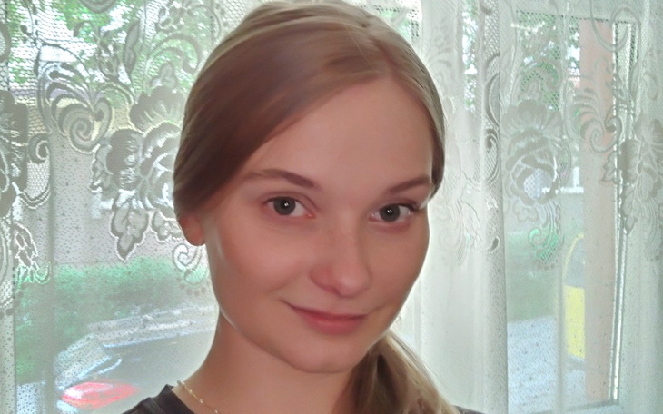 Portret młodej kobiety z uśmiechem, stojącej przy oknie.