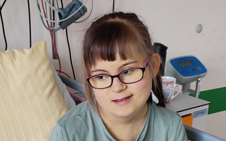 Młoda dziewczyna w szpitalu, nosząca okulary i uśmiechająca się.