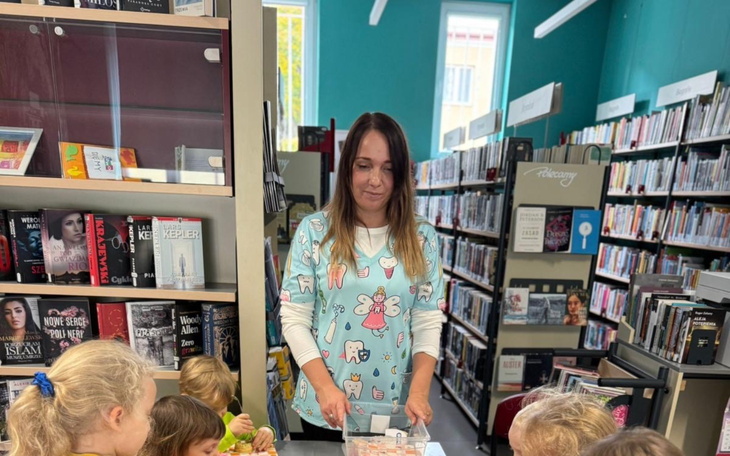 Kobieta w bibliotece z dziećmi, prowadząca zajęcia z książkami.