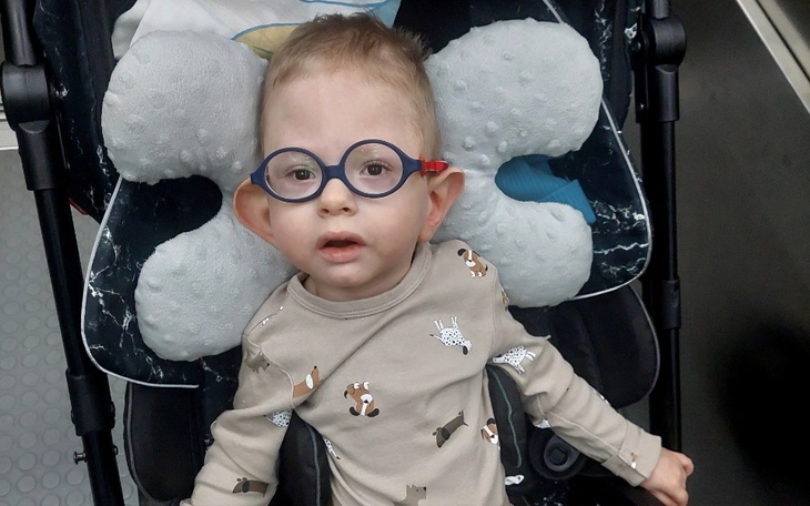 Mały chłopiec w okularach, siedzący w wózku dziecięcym.