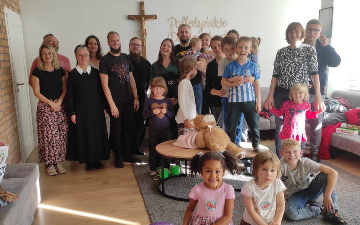 Grupa dzieci i dorosłych pozujących do zdjęcia w przytulnym wnętrzu.