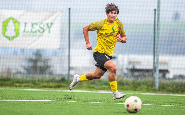 Młody piłkarz biegnący za piłką na boisku.