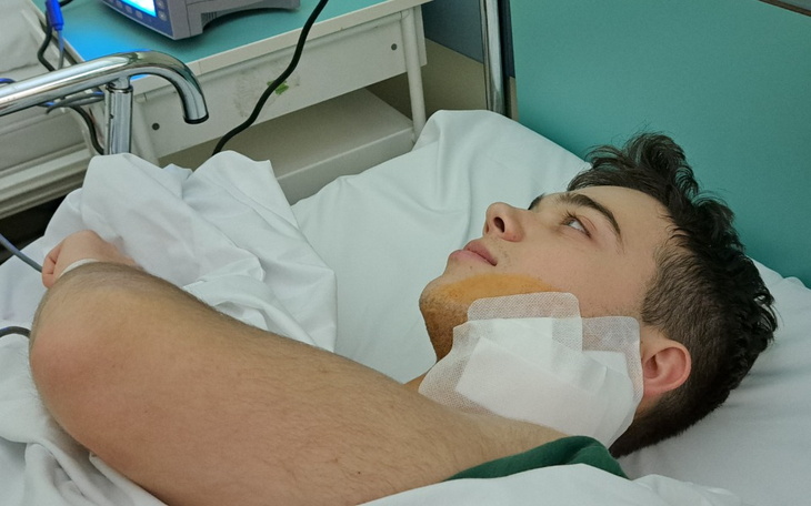 Młody mężczyzna leżący w szpitalnym łóżku, z opatrunkiem na szyi.