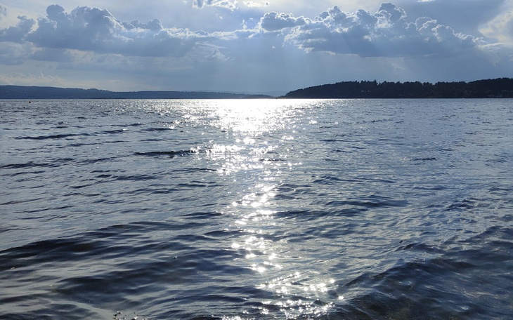 Widok na jezioro z promieniami słońca odbijającymi się w wodzie.