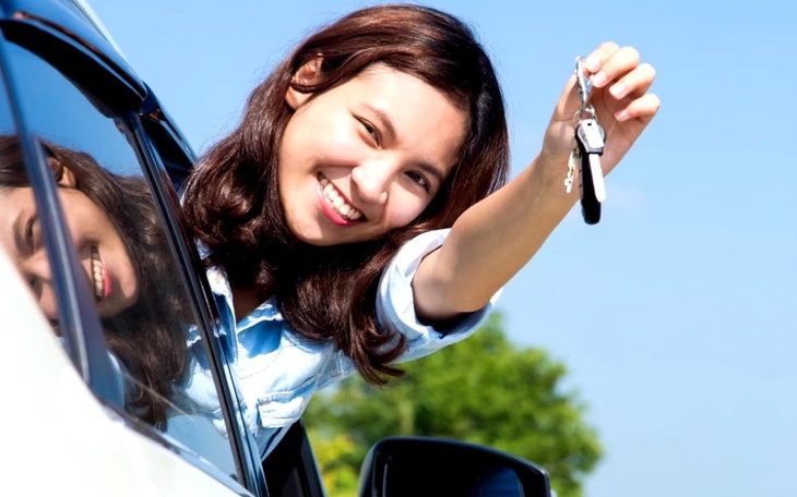 Kobieta w samochodzie, trzymająca kluczyki i uśmiechająca się.
