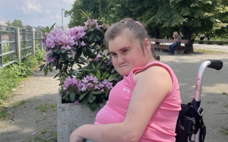 Dziewczynka w różowej koszulce siedzi obok kwitnących krzewów.