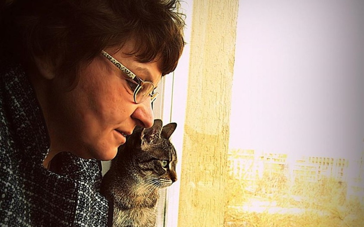 Kobieta z okularami i kotem, spoglądają na zewnątrz przez okno.