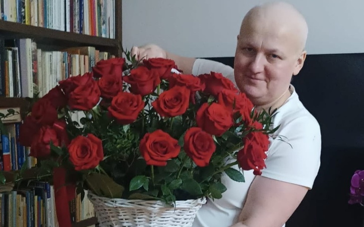 Osoba trzymająca bukiet czerwonych róż, uśmiechająca się.