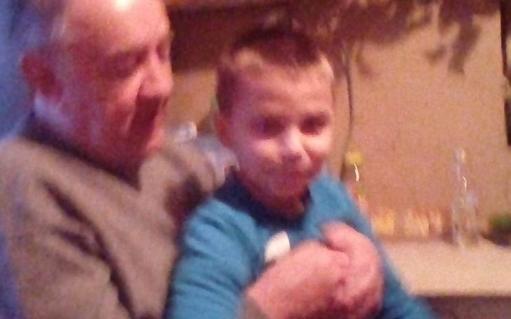 Dziecko w niebieskiej koszulce siedzi na kolanach starszego mężczyzny.