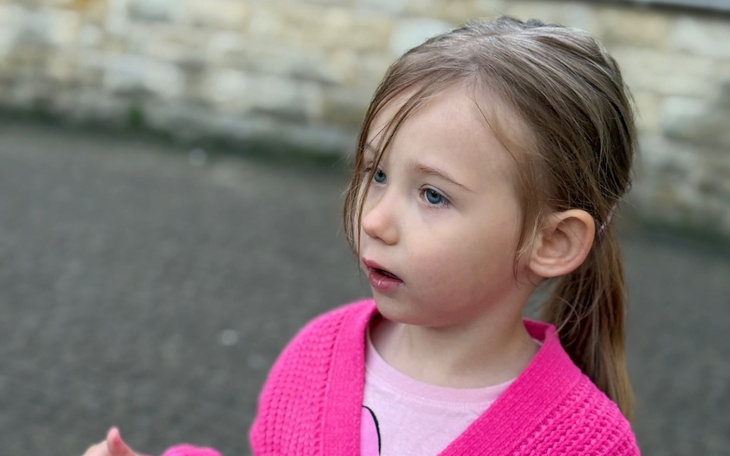Mała dziewczynka w różowym sweterku, zaintrygowana otoczeniem.