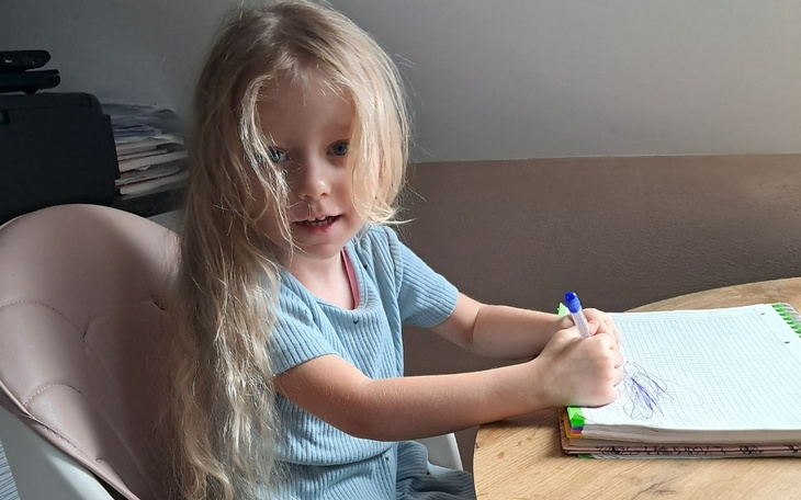 Mała dziewczynka rysująca na kartce przy stole.