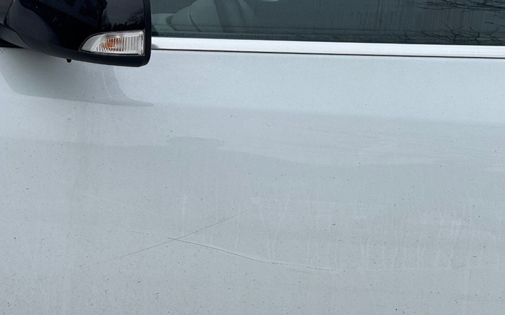 Zarysowanie na białym samochodzie, widoczne na drzwiach.