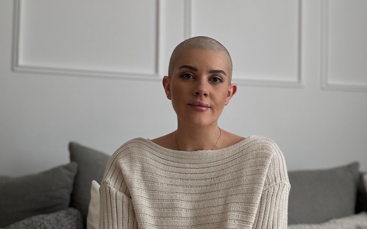 Kobieta z krótkimi włosami w jasnym swetrze siedzi na kanapie.