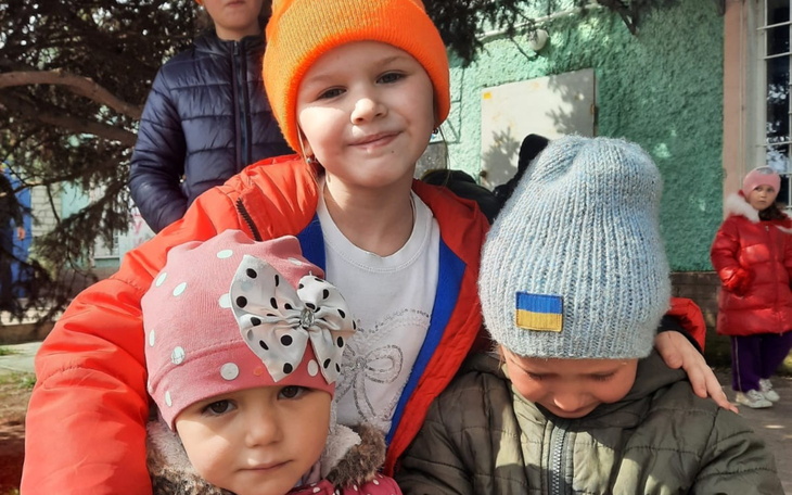 Trzy dzieci w kolorowych czapkach, uśmiechające się do kamery.