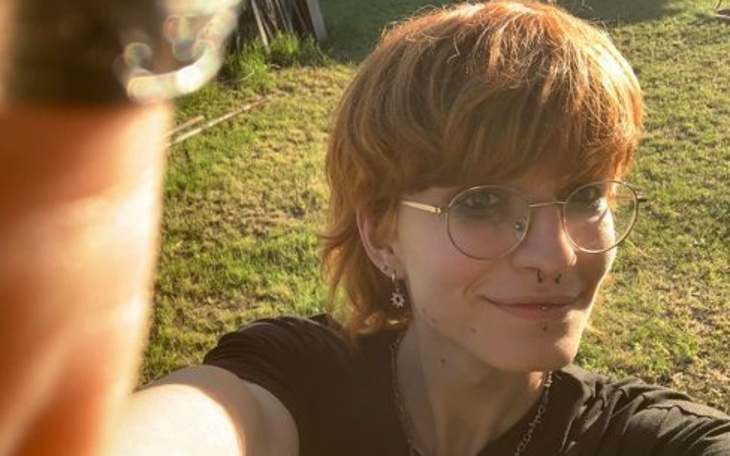 Osoba z okularami i kolczykami, robiąca selfie na zewnątrz.