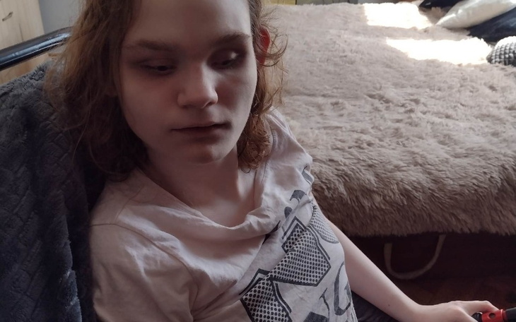 Młoda osoba siedząca na kanapie, z zamyślonym wyrazem twarzy.