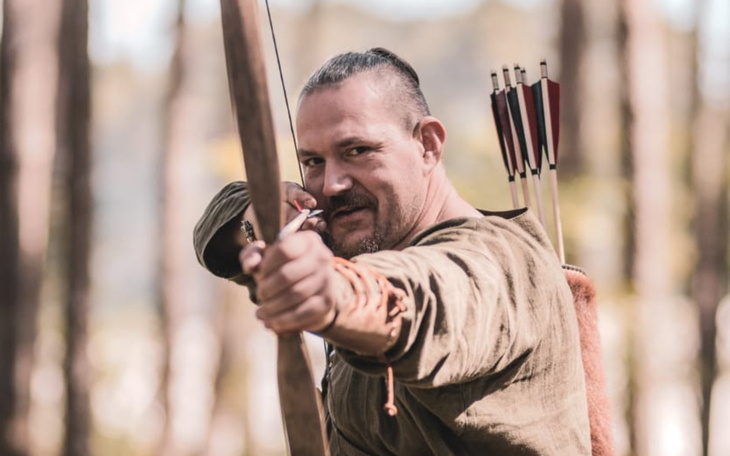 Mężczyzna z łukiem, gotowy do strzału w lesie.