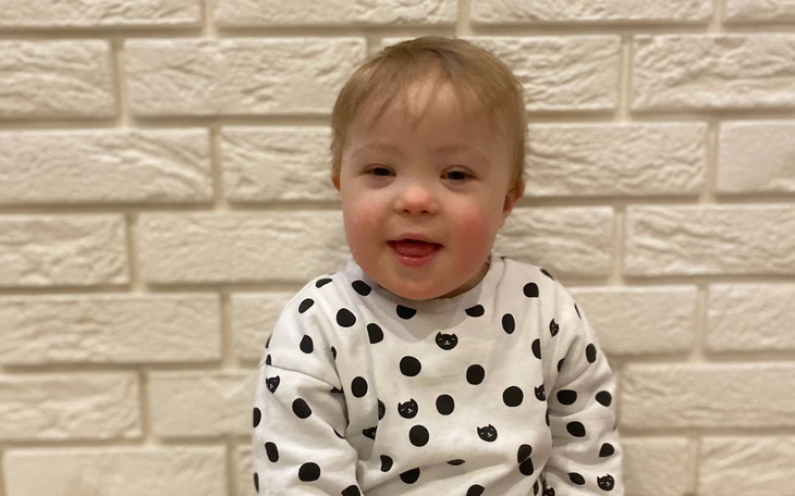 Uśmiechnięte dziecko w kropkowanej bluzie na tle ściany.