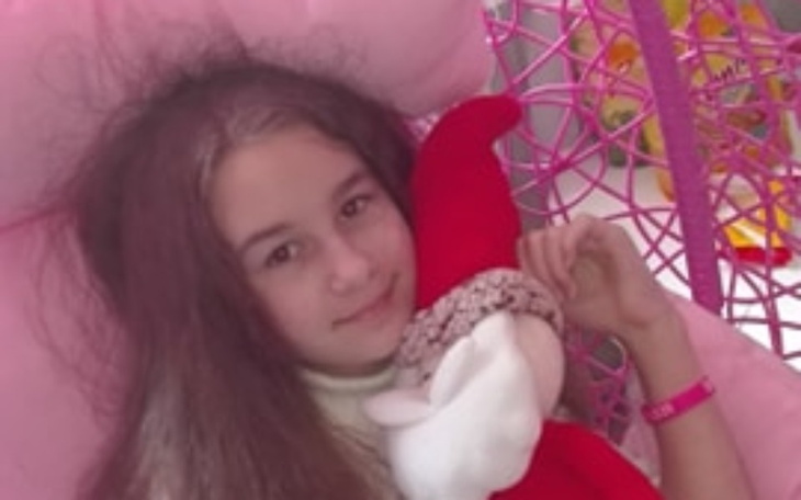 Dziewczynka z pluszowym misiem w różowym otoczeniu.