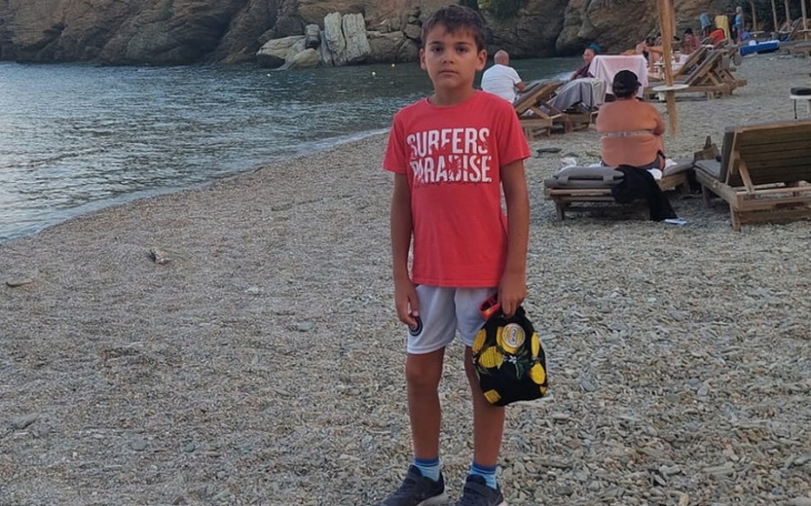 Chłopiec na plaży w czerwonej koszulce, trzyma torbę.