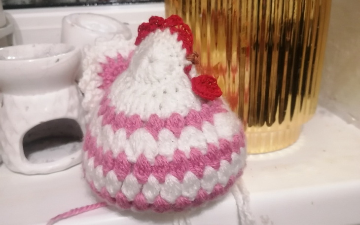 Ręcznie robiona, kolorowa kurka z włóczki na tle dekoracji.