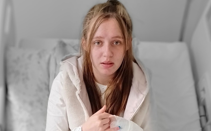 Młoda kobieta w szpitalu, trzymająca rękę na opatrunku.