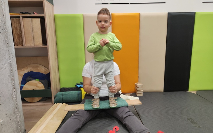 Dziecko stojące na kolanach dorosłego, w kolorowym otoczeniu.