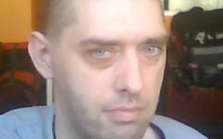 Mężczyzna z poważnym wyrazem twarzy, siedzi w pomieszczeniu.