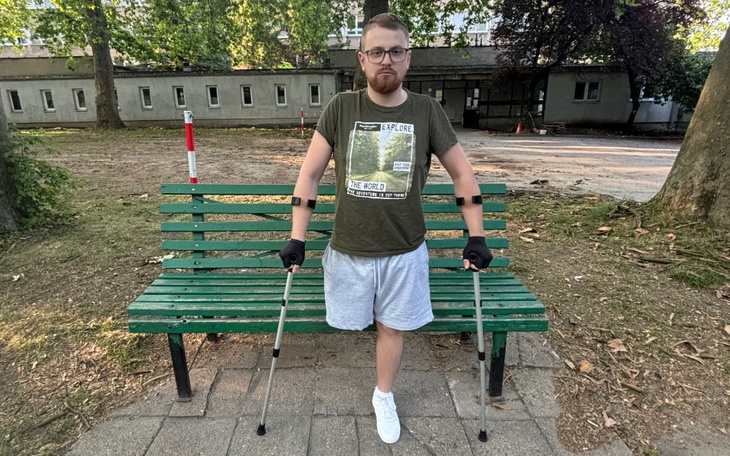 Mężczyzna na ławce z kulami, w zielonej koszulce, w parku.