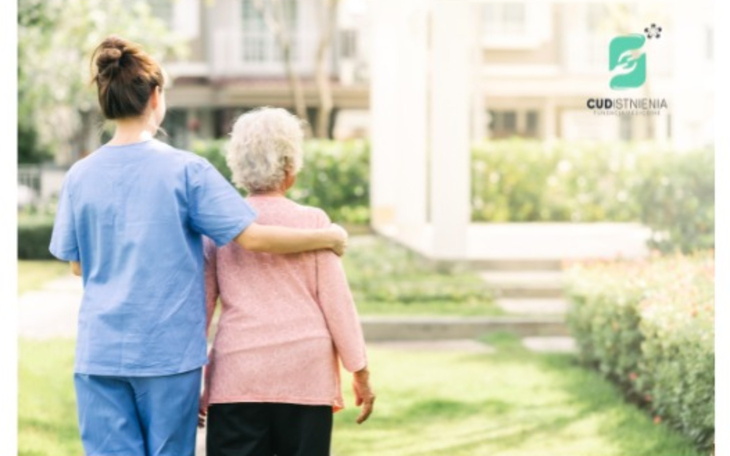 Pracownik opieki prowadzący starszą osobę na zewnątrz.