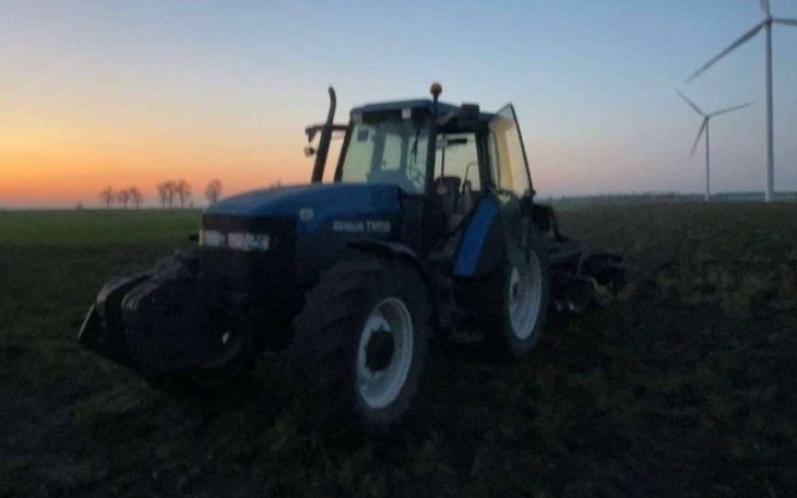 Traktor na polu przy zachodzie słońca, z wiatrakami w tle.