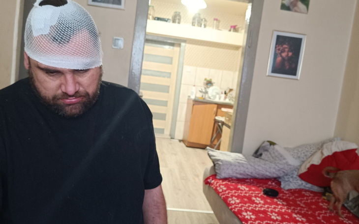 Mężczyzna z opatrunkiem na głowie, wygląda na zmartwionego.