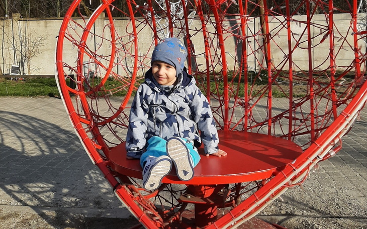 Dziecko siedzące na huśtawce w kształcie serca, uśmiechnięte.