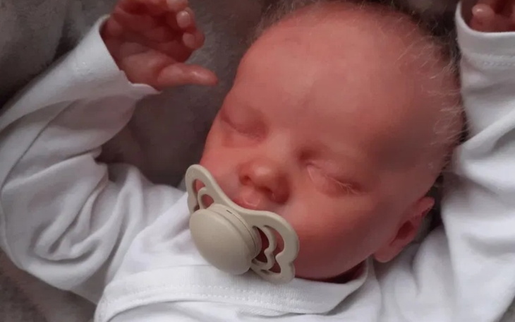 Noworodek śpiący z smoczkiem, w białym ubranku.