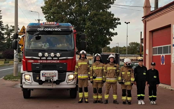 Strażacy w mundurach obok wozu strażackiego, gotowi do akcji.