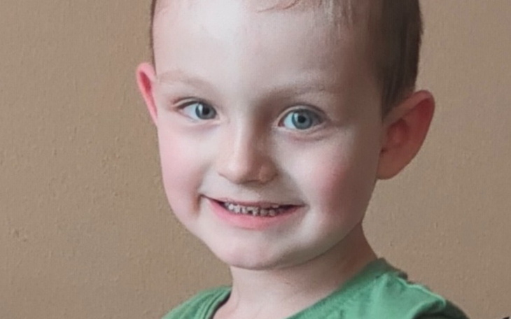 Uśmiechnięty chłopiec z niebieskimi oczami, w zielonej koszulce.