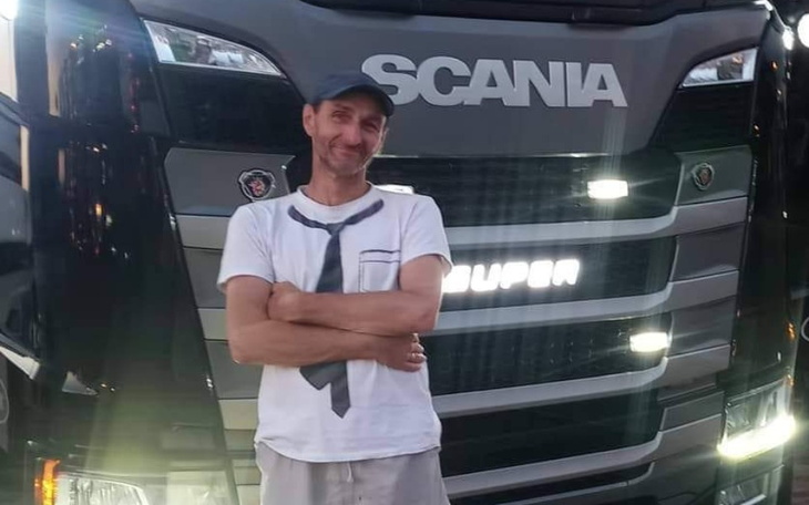 Mężczyzna stoi obok ciężarówki Scania, uśmiechając się.