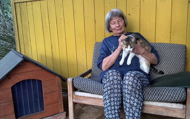 Starsza kobieta trzymająca kota, siedząca na tarasie.