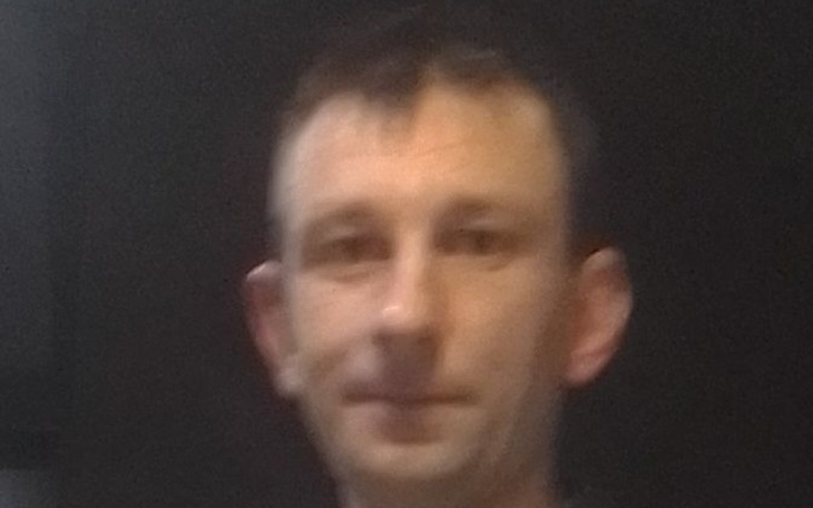 Mężczyzna w ciemnym pomieszczeniu, patrzy w obiektyw.