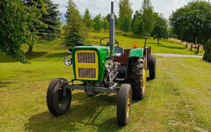 Traktor na zielonej łące, otoczony drzewami.