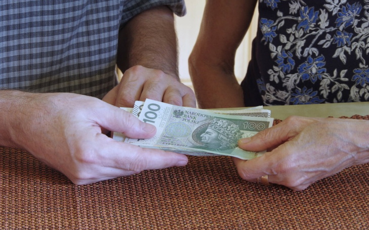 Dwie osoby przekazujące sobie pieniądze przy stole.