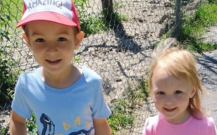 Dwoje dzieci uśmiecha się na tle ogrodzenia, spędzają czas na świeżym powietrzu.