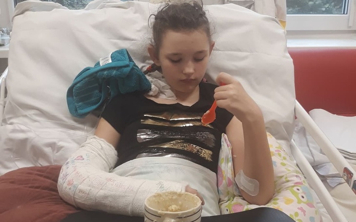 Dziewczynka w szpitalu, jedząca posiłek z unieruchomioną ręką.