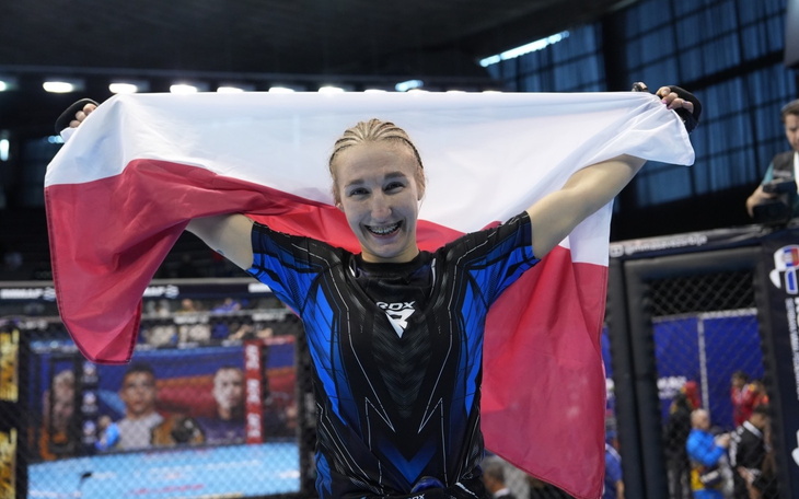 Zawodniczka MMA trzyma flagę Polski, uśmiechnięta po zwycięstwie.