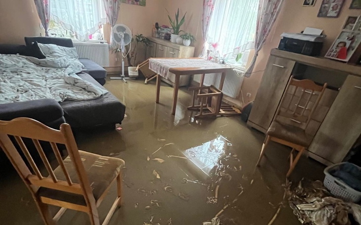 Zalane wnętrze domu po powodzi, z meblami w wodzie.