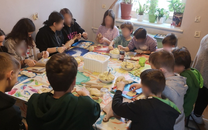 Grupa dzieci piekących ciasto przy stole w kuchni.